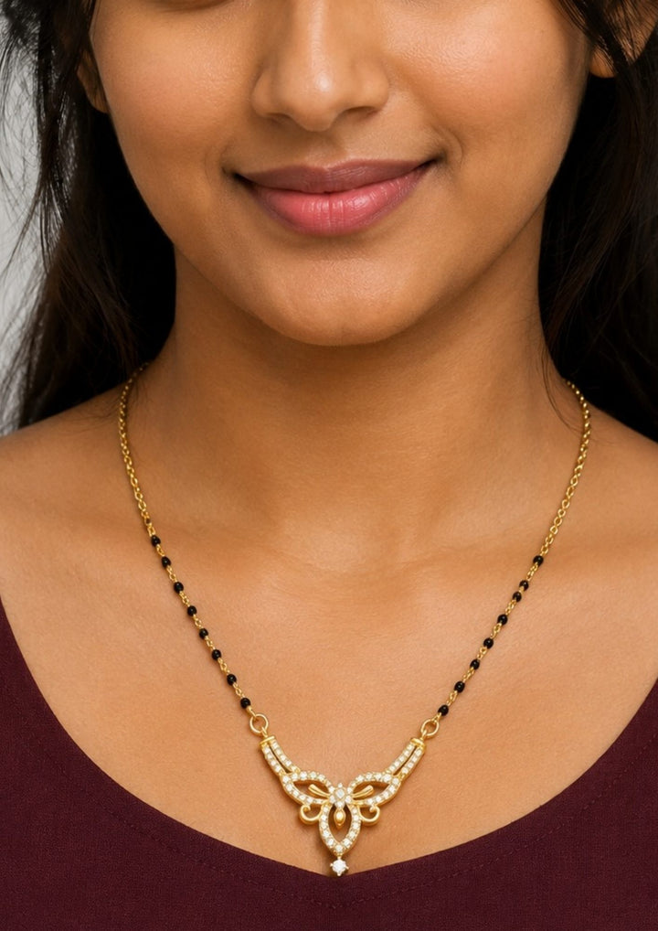 Woman wearing a gold necklace Modern Zircon Diamond gold plated mangalsutra necklace The design features a delicate gold link chain transitioning into sections of traditional small black beads on both sides. The central pendant showcases a sleek, contemporary curved V-shape and a stylized butterfly or floral motif encrusted with sparkling white cubic zirconia stones. This elegant neckpiece perfect for daily wear, office wear, and casual outfits. 