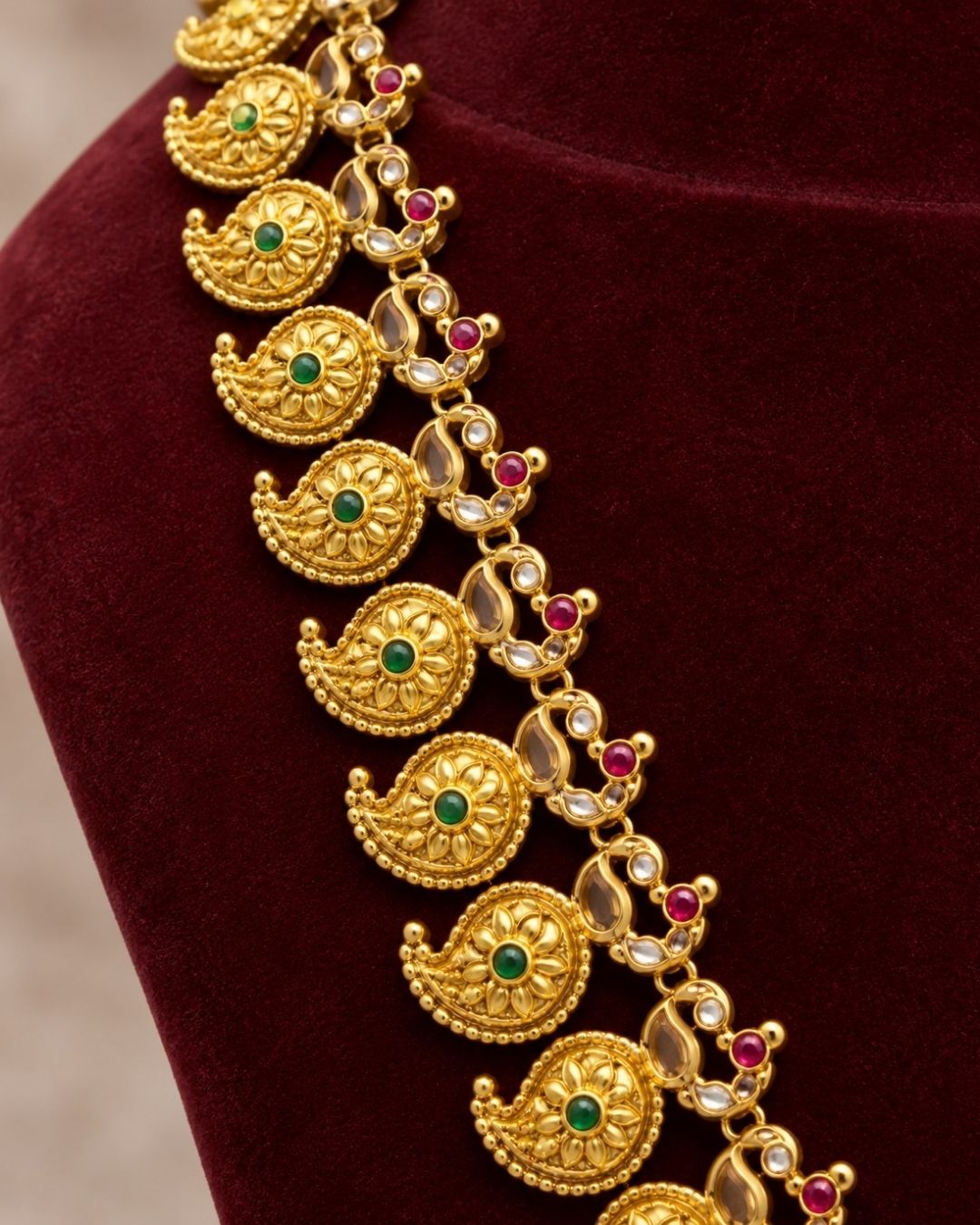 Elegant gold plated long haram featuring intricately crafted paisley motifs adorned with green and ruby stone accents, paired with matching earrings. Inspired by traditional South Indian temple jewellery, this timeless necklace set is perfect for weddings, bridal wear, festivals, and cultural celebrations.