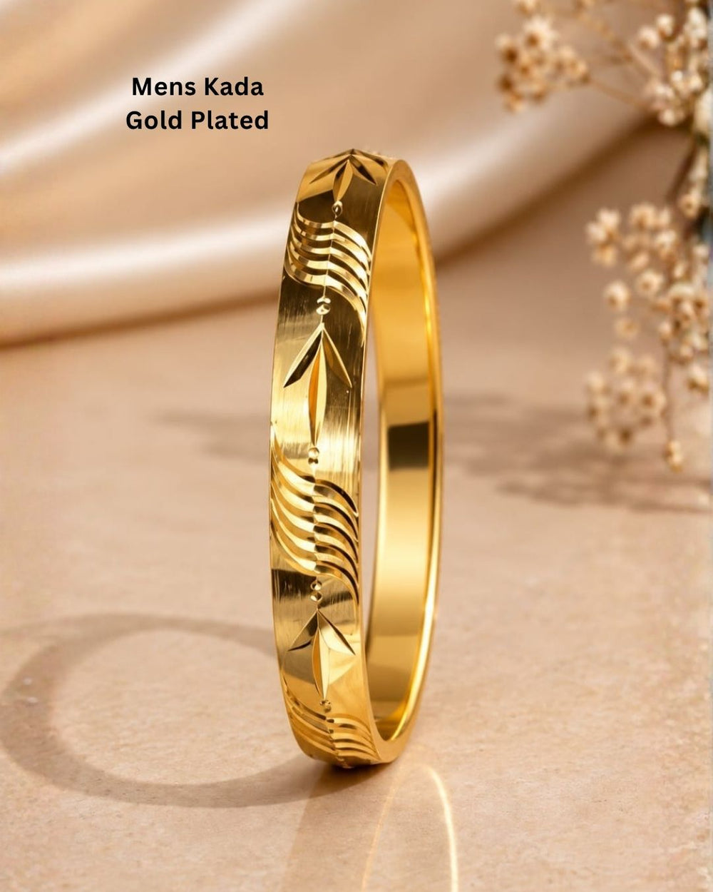 Gold plated men's kada displayed upright on a beige stone surface with a soft neutral background and delicate floral accents.