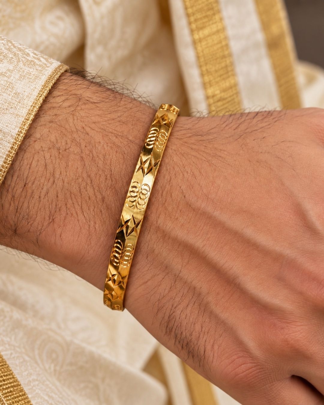 Gold plated men’s kada displayed upright on a dark wooden surface against a black background, highlighting its intricate geometric detailing.