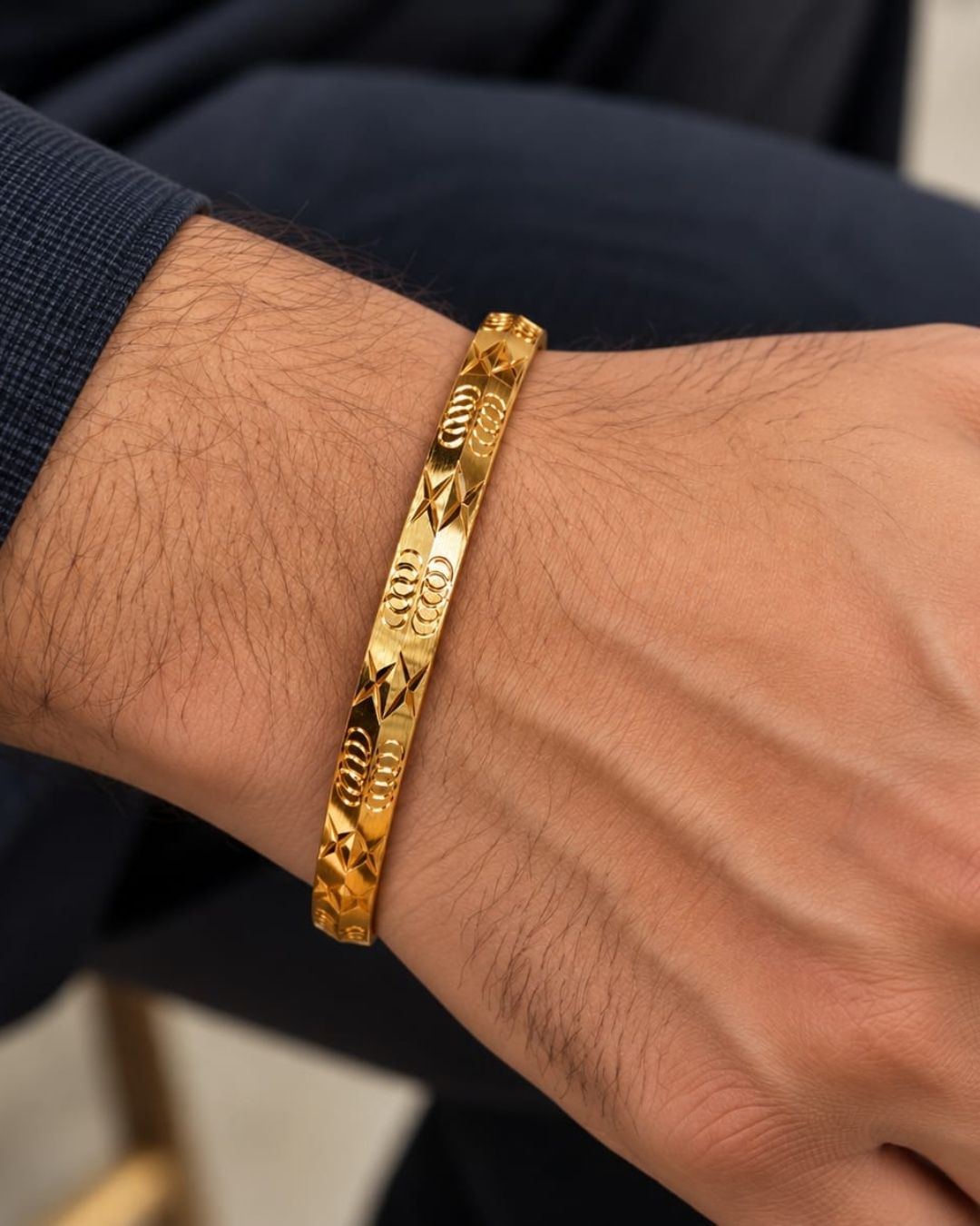 Gold plated men’s kada displayed upright on a dark wooden surface against a black background, highlighting its intricate geometric detailing.