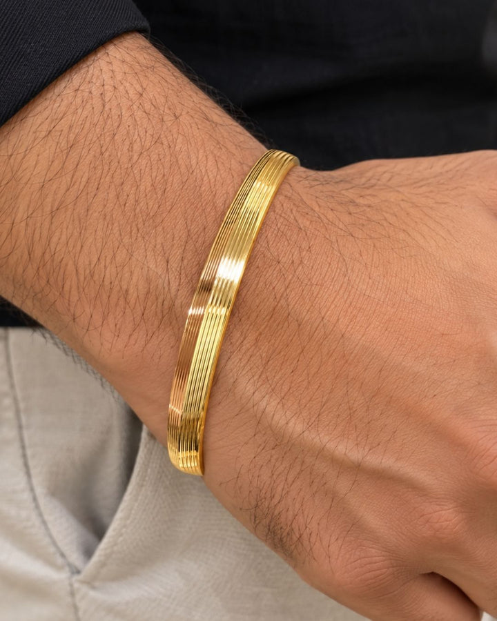 Stylish men’s gold plated kada displayed upright on a warm beige surface with a premium minimal background.