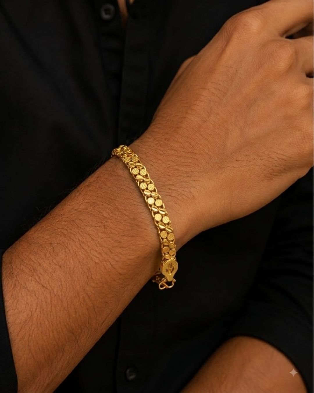 A close-up of a person's wrist wearing a textured, gold-toned tennis-style chain bracelet with a small lobster clasp, set against a black shirt.