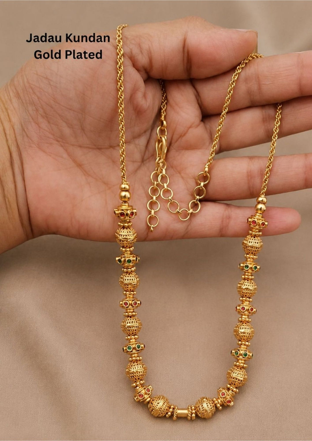 Gold plated long chain haraam necklace featuring elegant textured golden spheres alternating with small spacer rings inset with red ruby and green emerald stone accents. This lightweight chain is crafted with a detailed twisted rope style chain extension held in hand to provide a classy and premium appearance suitable for daily wear, office wear, casual outings, family gatherings, festivals, parties and traditional occasions with skin friendly quality, anti fade polish, comfortable fitting