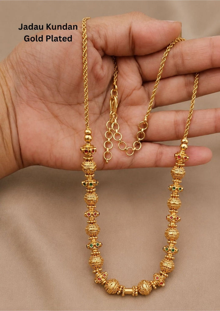 Gold plated long chain haraam necklace featuring elegant textured golden spheres alternating with small spacer rings inset with red ruby and green emerald stone accents. This lightweight chain is crafted with a detailed twisted rope style chain extension held in hand to provide a classy and premium appearance suitable for daily wear, office wear, casual outings, family gatherings, festivals, parties and traditional occasions with skin friendly quality, anti fade polish, comfortable fitting