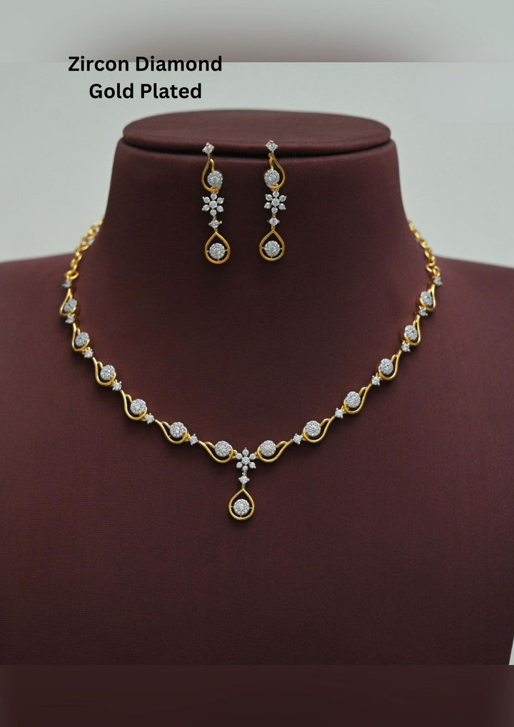 A sleek zircon diamond gold plated necklace set  features a delicate, undulating gold wave chain studded with round-cut sparkling white stones, transitioning into a central floral accent and a hanging open-teardrop solitaire pendant with matching dangling earrings.