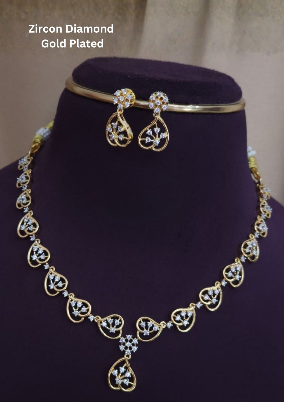 The necklace features a delicate chain composed of linked, hollow heart or leaf-shaped gold frames encrusted with small white zircon diamonds. The center drops into a subtle floral cluster and teardrop pendant, perfectly paired with a matching set of hanging drop earrings . Perfect for weddings, receptions, parties, functions and gifting.