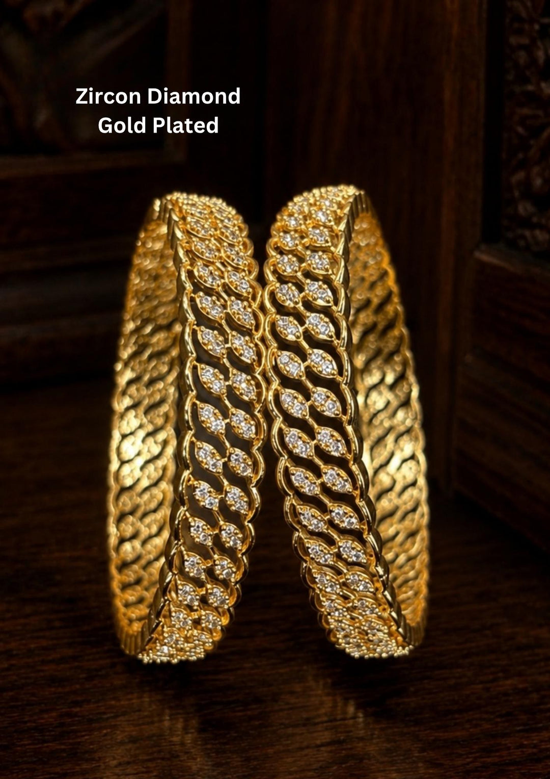 A sophisticated pair of sleek gold-plated bangles embellished with shimmering white Zircon diamonds. The design features a continuous, intertwining wave or leaf-like pattern intricately handset with sparkling crystals for a diamond-like brilliance. ideal for parties and special occasions.