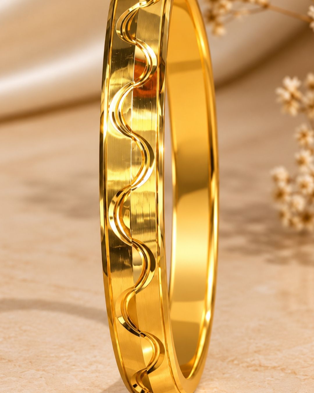 Gold plated men’s kada displayed upright on a beige surface, showcasing its modern wave pattern and reflective finish.