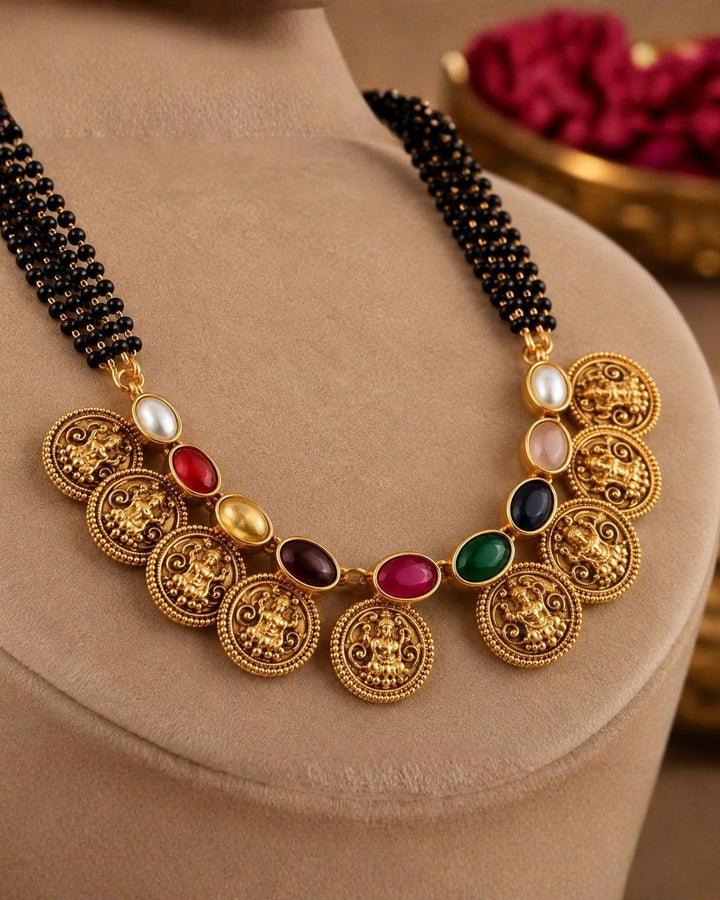 18k gold plated mangalsutra featuring a multi-strand black bead chain connected to a crescent of gold Lakshmi coins interspersed with colorful Navaratna gemstones. Includes matching gold Lakshmi coin earrings.