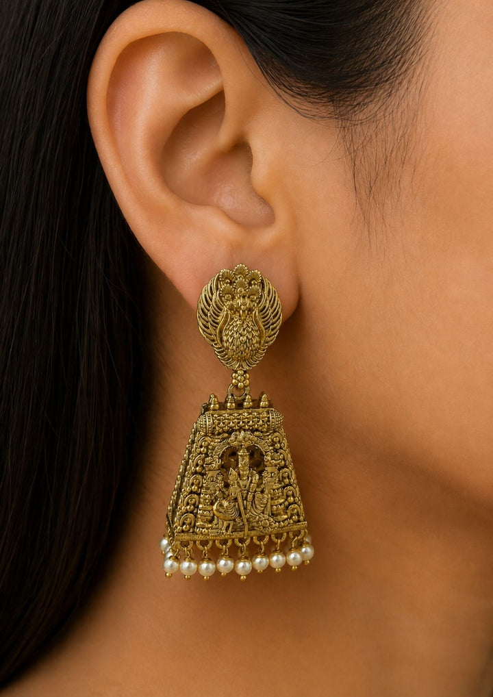 Close up of south indian women ear wearing Gold-plated Murgan jhumkas gold plated temple earrings designed with peacock and lord murgan in sitting position, traditional South Indian style, hanging white pearl drops, suitable for weddings, temple functions, festivals, Bharatanatyam, sarees, lehengas, and ethnic festive wear with rich royal appearance.