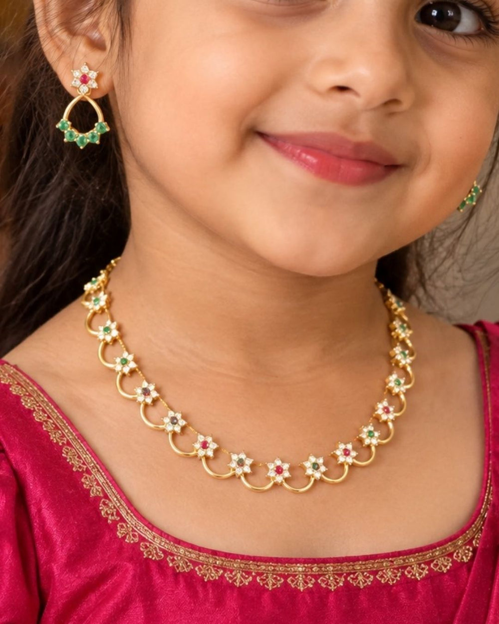 A delicate, lightweight 18k gold plated festive choker necklace featuring a continuous arrangement of scalloped open arch links. Each golden loop is centered with a shimmering clear zircon flower motif and alternating ruby-red and emerald-green stone centers, paired with matching dangling floral ear studs on a black presentation bust.