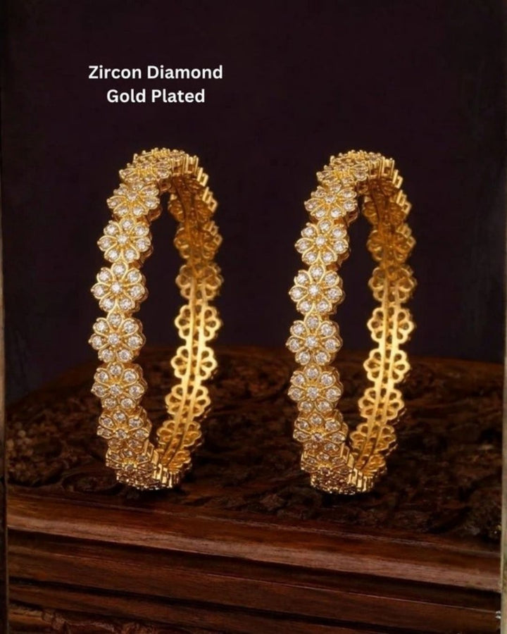 A pair of gold-plated bangles decorated with clear zirconia stones in a floral pattern, Beautiful zircon diamond gold plated floral bangles featuring continuous sparkling flower motifs and premium craftsmanship. Perfect for weddings, festivals, parties, and elegant everyday styling.
