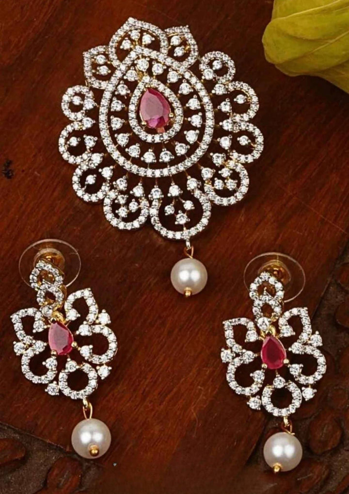 Elegant zircon diamond gold plated pendant set featuring a floral-inspired pendant designed with sparkling white zircon stones arranged in circular patterns. The centerpiece showcases a pear-shaped emerald red stone surrounded by dazzling zircon stones, finished with a delicate pearl drop. The matching earrings mirror the same floral design with green stone and pearl danglers, Perfect for weddings, festivals, office wear, functions and its anti fade color