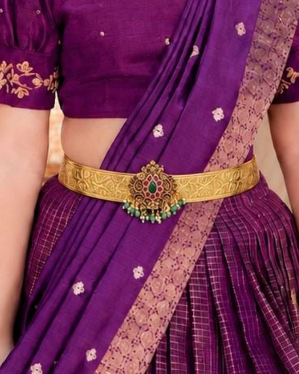 Beautiful gold plated kid’s hip belt featuring a wide intricately engraved band with a floral gemstone centerpiece decorated with ruby, green stones, and pearl drops. Perfect for children’s traditional wear, weddings, festive occasions, cultural events, parties, and gifting.