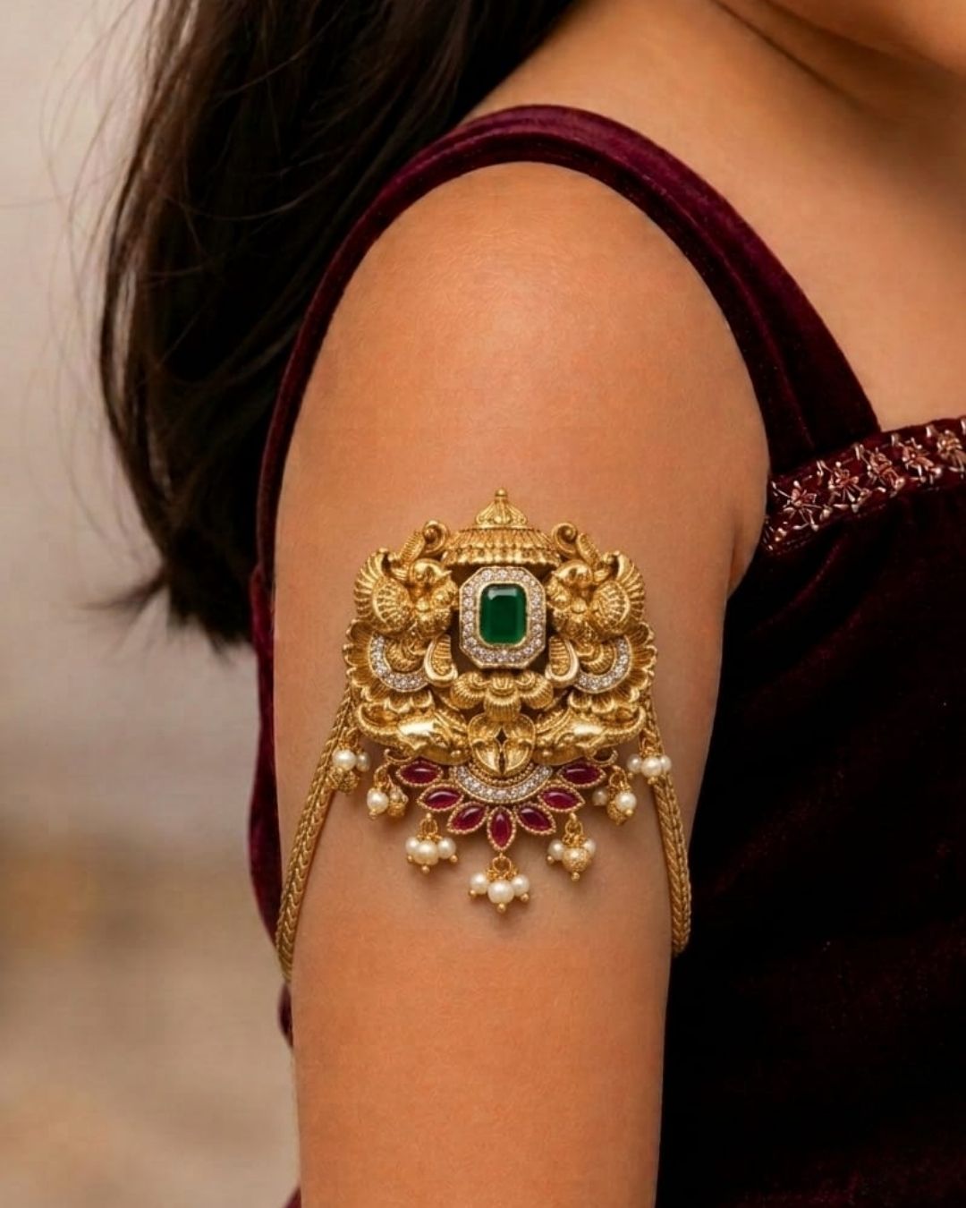 Beautiful gold plated kids vanki featuring an intricately crafted traditional design with a large green stone centerpiece, sparkling clear stones, ruby floral motifs, and elegant pearl drops. Perfect for traditional wear, weddings, festivals, classical dance, special occasions, and gifting.
