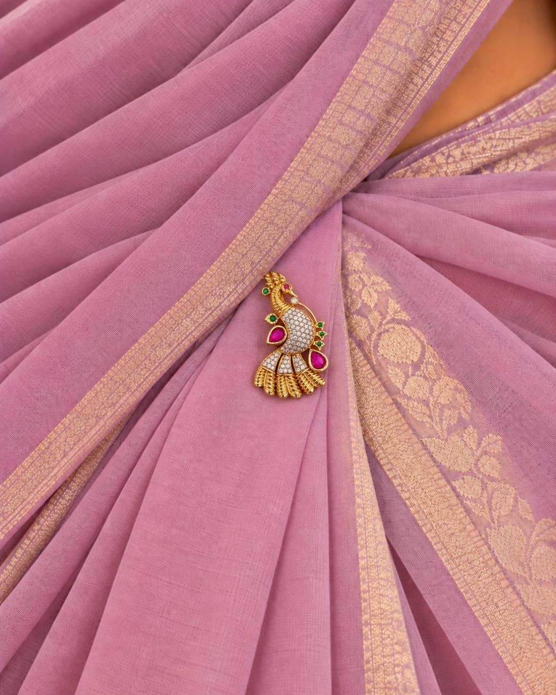 Pair of gold plated peacock saree pins displayed on a light wooden surface, showcasing detailed craftsmanship and decorative stone embellishments.