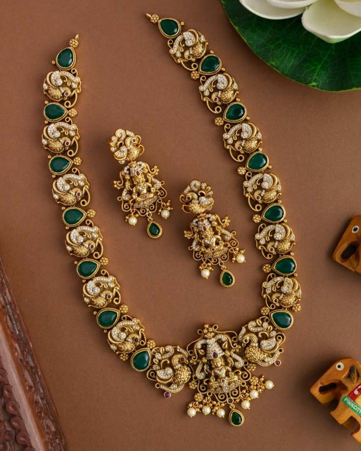 Premium antique gold plated temple necklace and earrings set crafted with intricate Ganesha and peacock designs, sparkling CZ stones, green accents, and elegant pearl details.