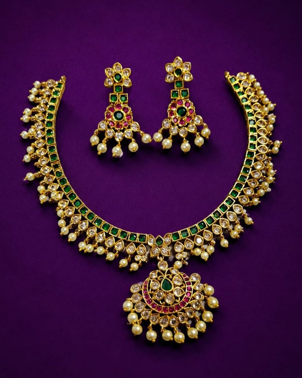 Beautiful gold plated necklace and earrings set featuring intricate green stone detailing, sparkling white stones, pink accents, and multiple pearl drops. Perfect for weddings, festive occasions, traditional outfits, celebrations, and elegant gifting.