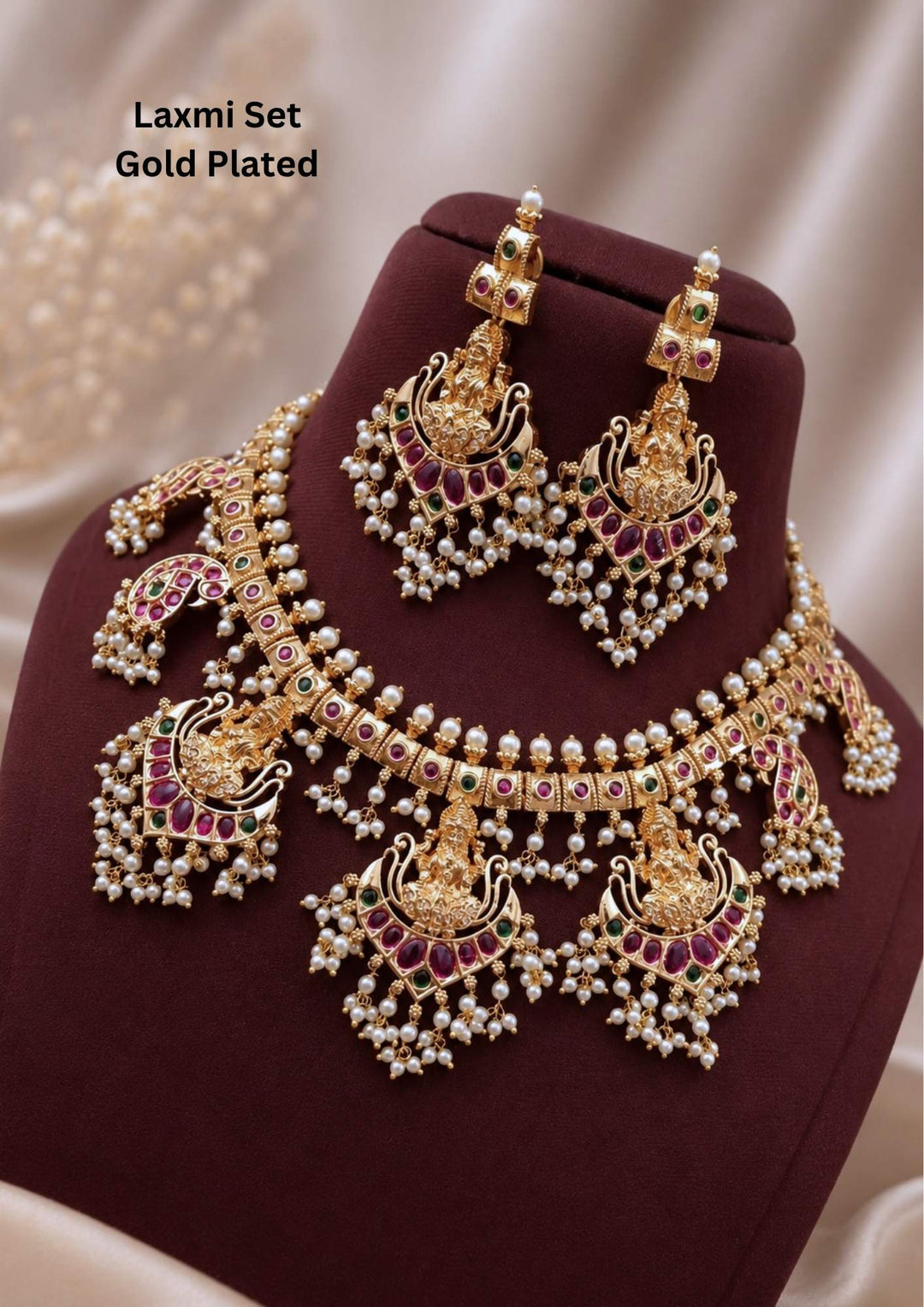 Gold plated temple jewelry set featuring a choker band adorned with pink kundan stones and tiny white pearls, leading down to multiple hanging crescent pendants embossed with Laxmi Devi motifs. The entire piece is finished with dense clusters of dangling white pearl beads. Includes matching grand hanging earrings with a similar Laxmi Devi design. Perfect for weddings and festivals with skin-friendly premium quality