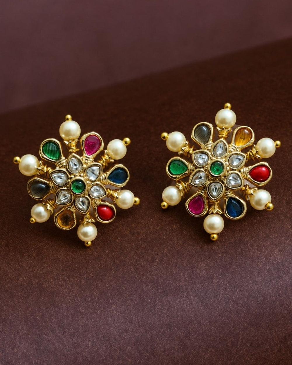 Beautiful Navratna pearl gold plated stud earrings featuring intricate floral craftsmanship, multicolor gemstone accents, sparkling white stones, and elegant pearl detailing. Perfect for weddings, festive occasions, traditional outfits, temple visits, and premium gifting.