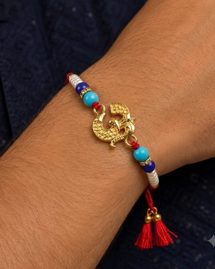 Premium spiritual Rakhi showcasing a gold finish Om Ganesha charm accented with blue beads, pearl beads, and a vibrant red thread.