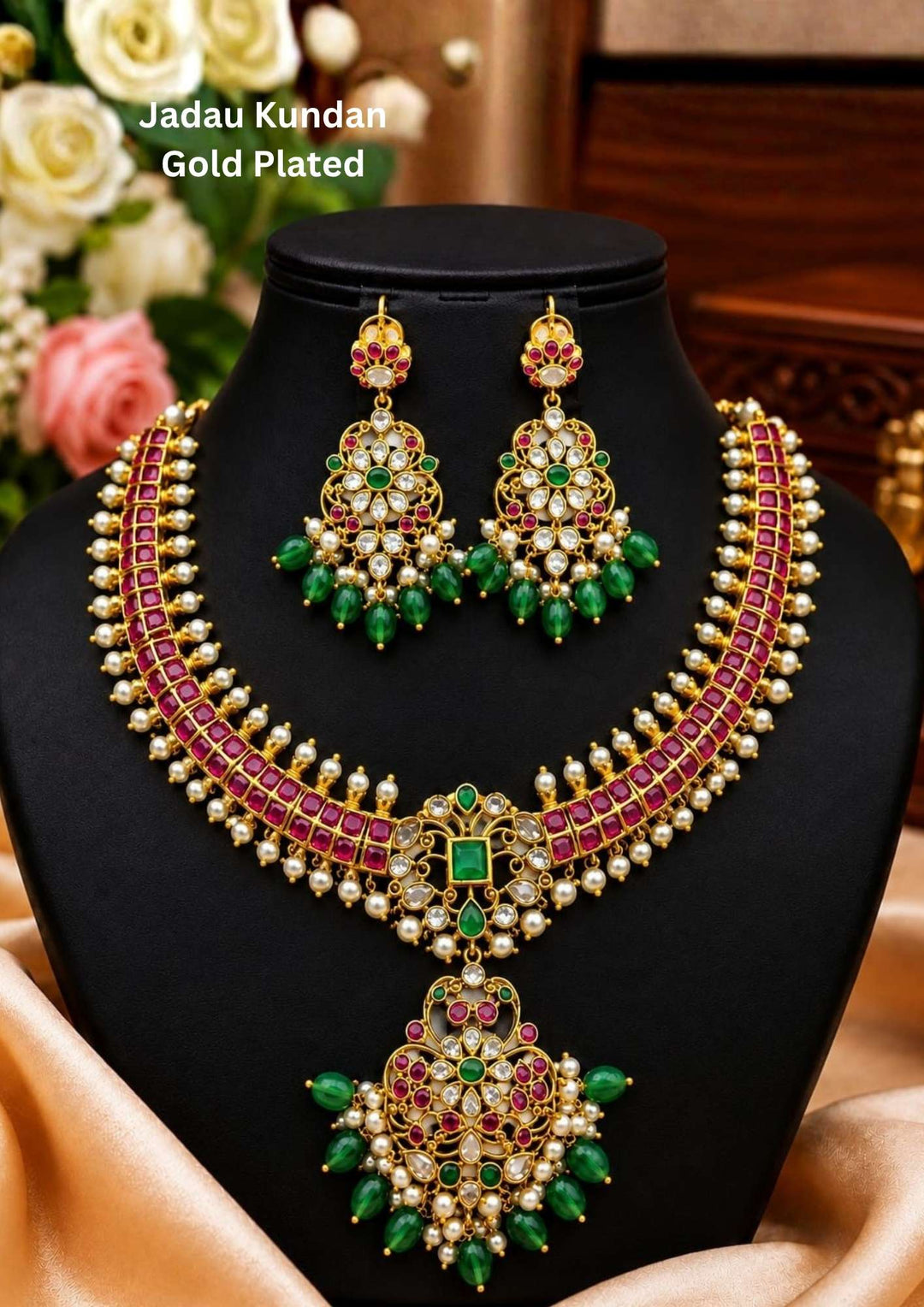 Traditional jadau kundan gold plated choker necklace set featuring a stunning row of ruby-colored stones bordered with delicate pearl accents. The centerpiece showcases intricate kundan craftsmanship with sparkling white stones, vibrant green gemstone details and an ornate pendant adorned with pearl clusters and emerald green bead drops. The matching chandelier earrings mirror the necklace design, creating a luxurious bridal and festive look.