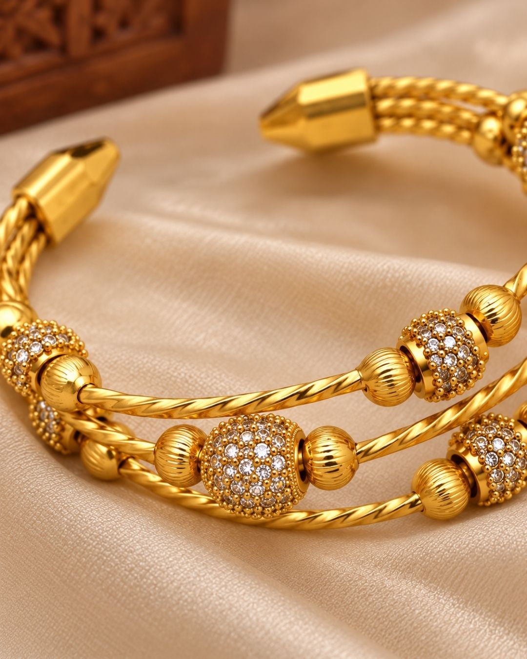 Gold plated adjustable kada for women featuring a triple twisted design, decorative gold beads, and sparkling white stone embellishments.