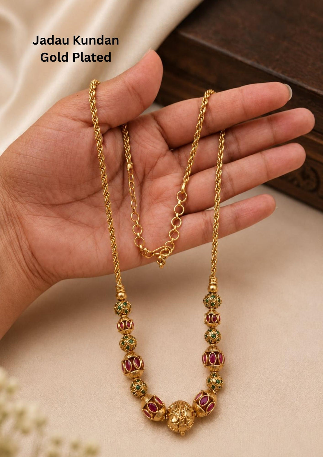 Gold plated long chain haraam necklace featuring elegant textured golden spheres alternating with small spacer rings inset with red ruby and green emerald stone accents. This lightweight chain is crafted with a detailed twisted rope style chain extension held in hand to provide a classy and premium appearance suitable for daily wear, office wear, casual outings, family gatherings, festivals, parties and traditional occasions with skin friendly quality, anti fade polish, comfortable fitting