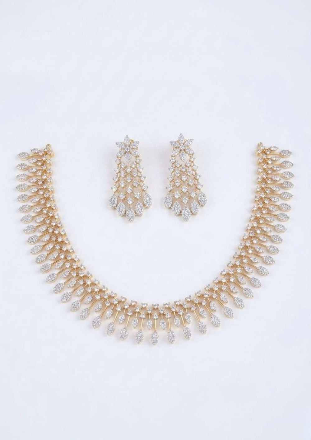 Elegant zircon diamond gold plated necklace set featuring a graceful collar-style necklace adorned with sparkling white zircon stones and cascading leaf-shaped dangling motifs. The matching statement earrings showcase a floral-inspired top with intricate stone-studded lattice detailing and shimmering leaf drops, creating a luxurious and sophisticated look suitable for weddings, receptions, parties and festive occasions.