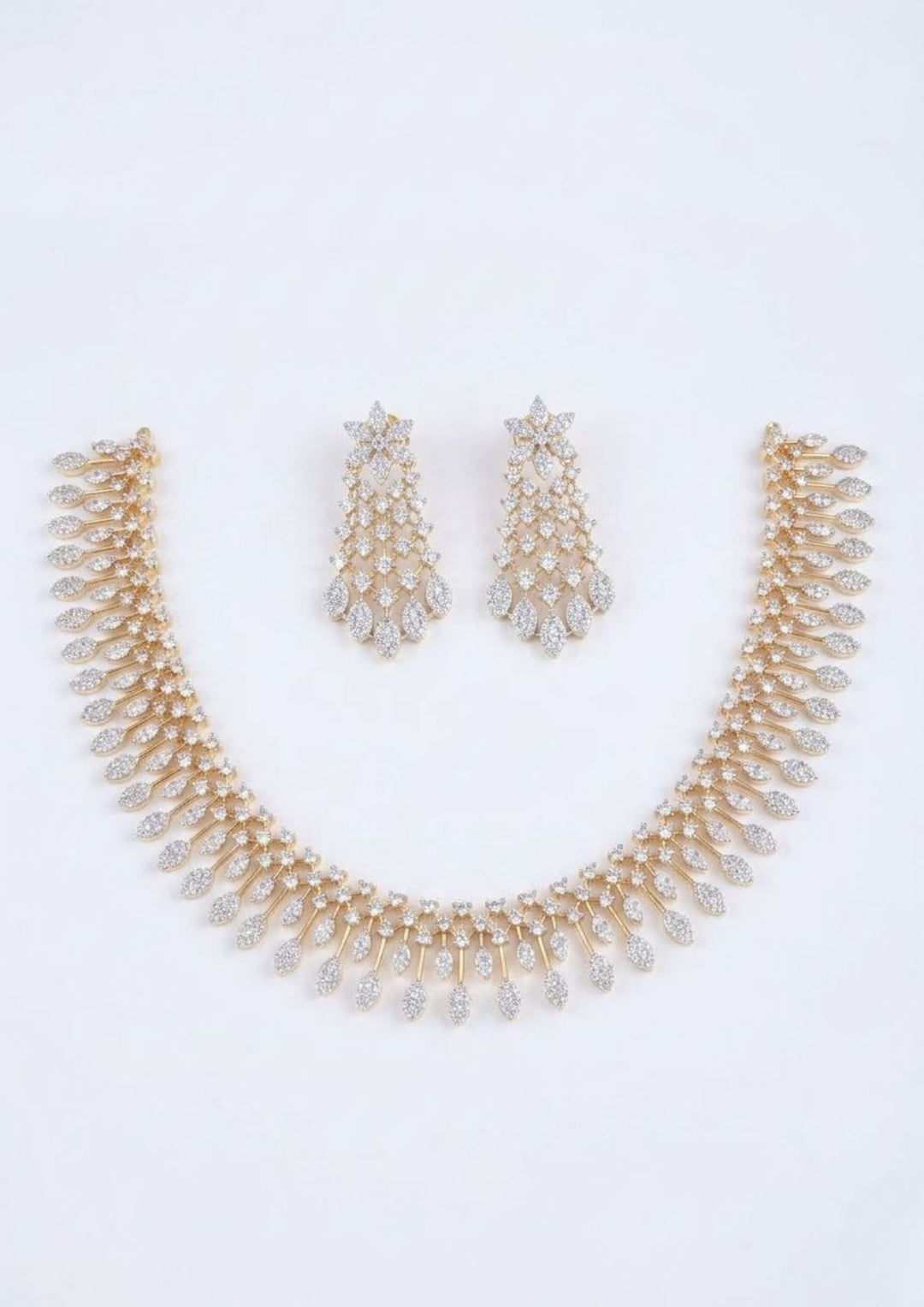 Elegant zircon diamond gold plated necklace set featuring a graceful collar-style necklace adorned with sparkling white zircon stones and cascading leaf-shaped dangling motifs. The matching statement earrings showcase a floral-inspired top with intricate stone-studded lattice detailing and shimmering leaf drops, creating a luxurious and sophisticated look suitable for weddings, receptions, parties and festive occasions.