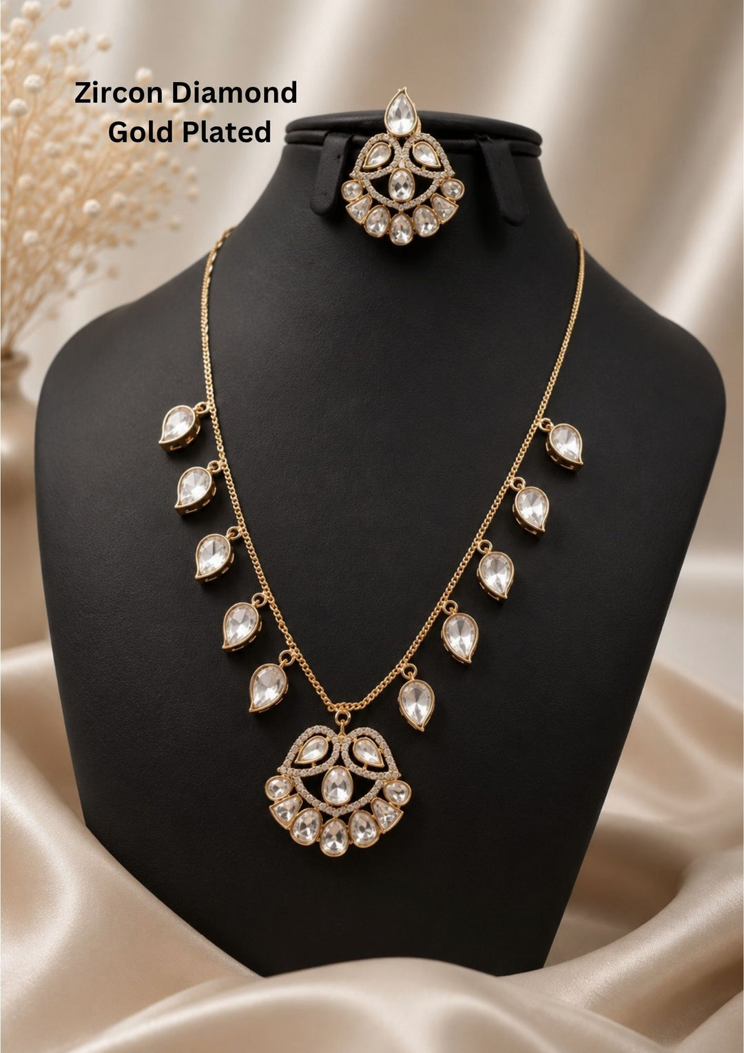 gold plated jewelry set featuring a delicate gold link chain spaced out with dangling tear-drop shaped pure zirconian diamonds, leading down to a crescent-style fan pendant filled with matching clear diamond stones. The set comes with a coordinating matching tear-drop maang tikka. Perfect for weddings, festivals, poojas, and family celebrations with skin-friendly quality, comfortable fitting,