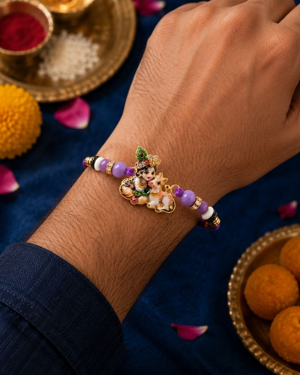A close-up of a person's wrist wearing a beaded Rakhi bracelet with a central deity charm, set against a festive dark blue cloth with gold bowls and flower petals.