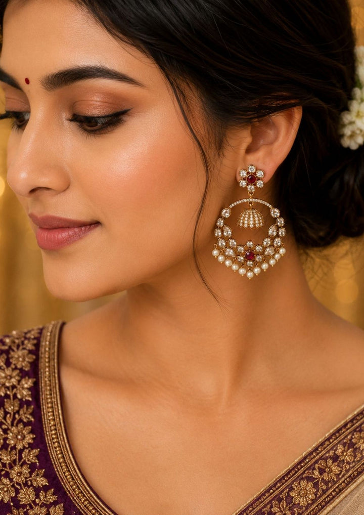 South indian women weaing Zircon diamond gold plated green Chandbali Long Earrings with hanging guttapusalu design, sparkling red zircon stones, floral pattern detailing, and elegant layered arrangement finished with shiny gold plating. The earrings come with lightweight, sweat proof quality, anti-fade colour, skin-friendly finish, and are suitable for weddings, receptions, festivals, functions, and party wear .