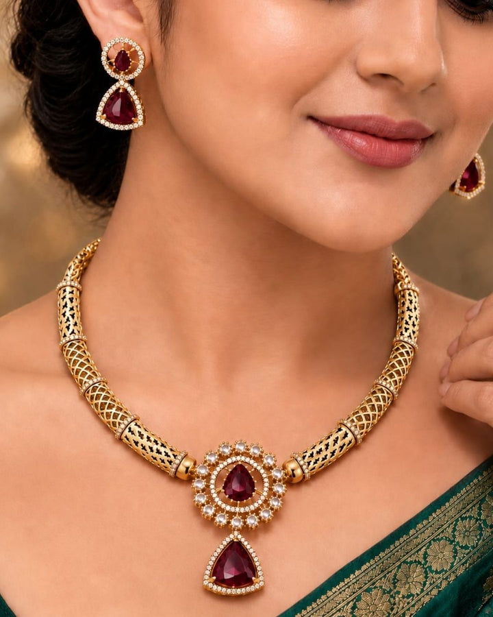South indian women Gold-plated necklace and matching earrings set displayed on a black jewelry bust. The necklace features a textured gold chain with a central teardrop pendant and matching drop earrings, embellished with green stones and small clear stones.