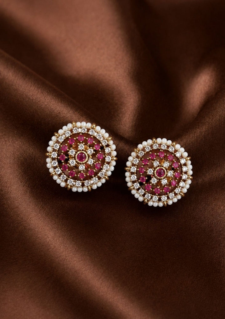 Elegant Jadau Kundan gold-plated stud earrings styled with traditional floral cluster patterns, with Ruby Pink stone settings, and a pearl halo. Perfect for festive celebrations, weddings, ethnic wear, and luxury gifting.