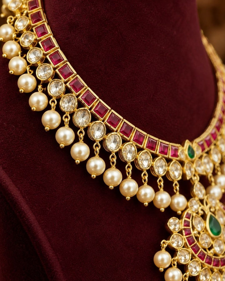Traditional style 18K gold plated choker necklace set designed with a red stone border band, white crystal outlines, a central crescent pendant, and clean rows of hanging white pearl drops that give a neat traditional look for festive celebrations, poojas, and weddings.