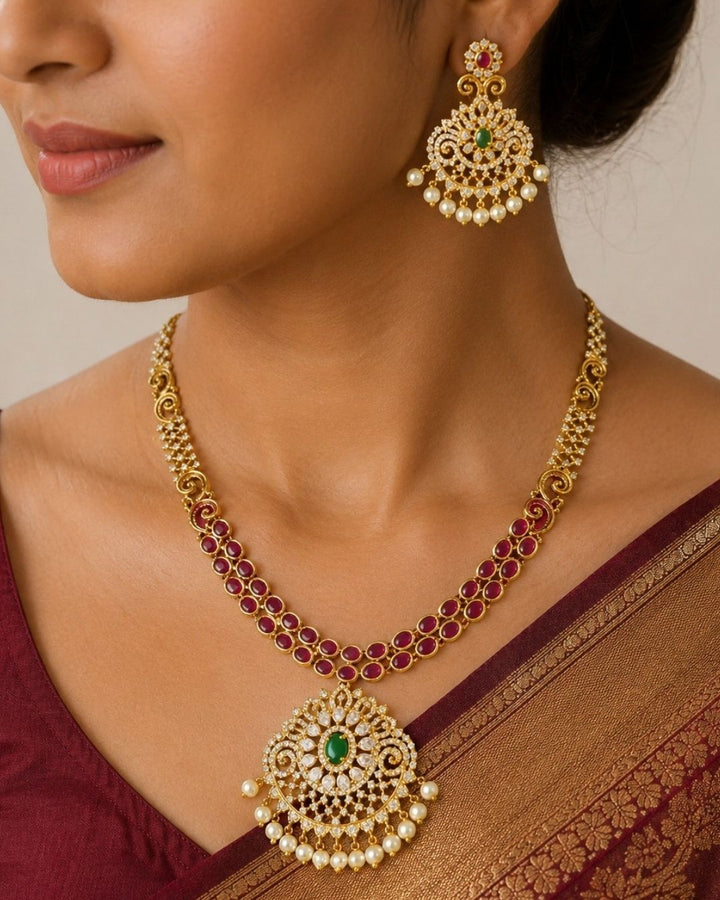 Premium gold plated CZ jewelry set with a ruby stone necklace, floral pendant, emerald green accents, pearl embellishments, and matching earrings for weddings and parties.