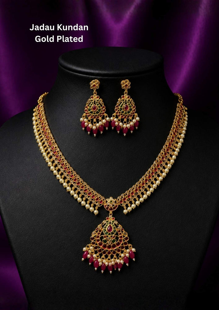 Beautiful Jadau Kundan gold plated pearl pendant necklace set featuring ruby and green stones, intricate kundan craftsmanship, pearl accents, and matching earrings. Perfect for weddings, festivals, temple visits, traditional outfits, bridal wear, and premium gifting.