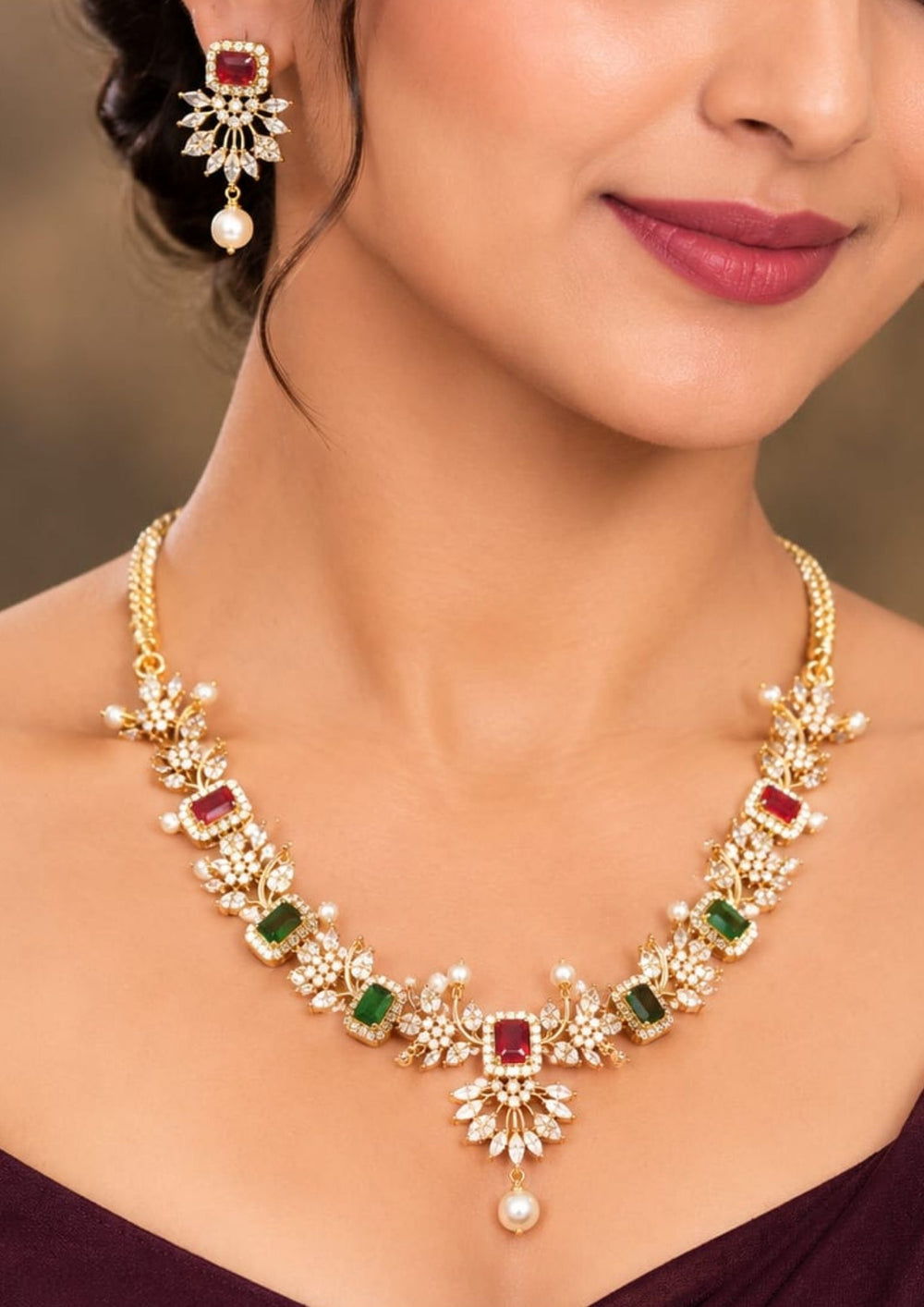 South indian women's Gold-plated Navratna jewelry set featuring a necklace and matching earrings The set is adorned with gold-plated floral motifs, green rectangular stones, pink rectangular stones, and white pearl-like drops. Elegant Navaratna gold plated necklace set featuring colorful gemstone-inspired stones, pearl drops, and matching earrings for festive occasions.