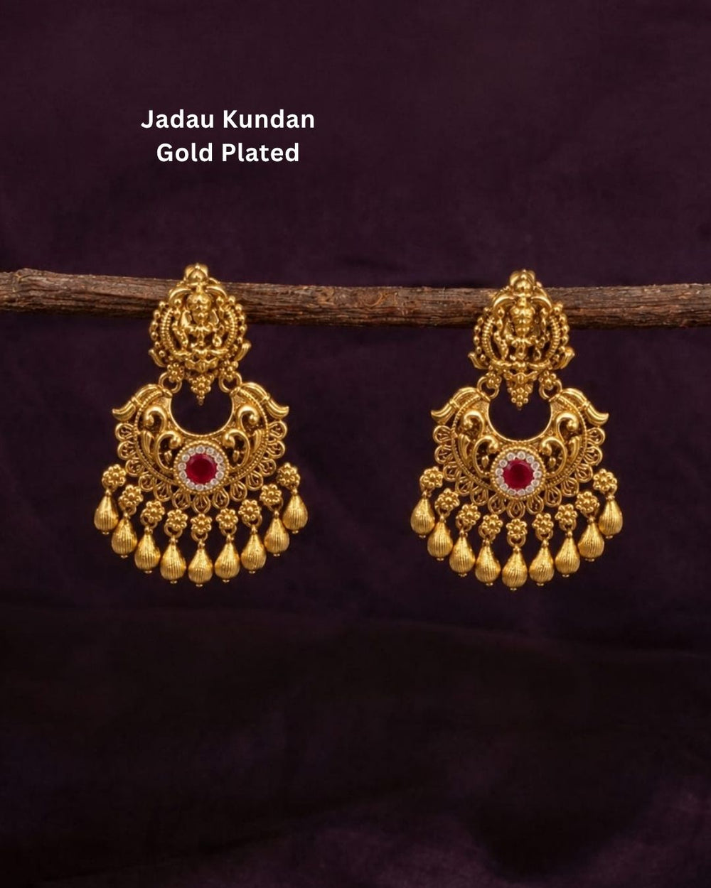 Gold-plated Laxmi Set jewelry necklace and matching earrings displayed on a dark red velvet bust. The necklace features intricate gold filigree, red and green stone accents, and rows of white faux pearls.