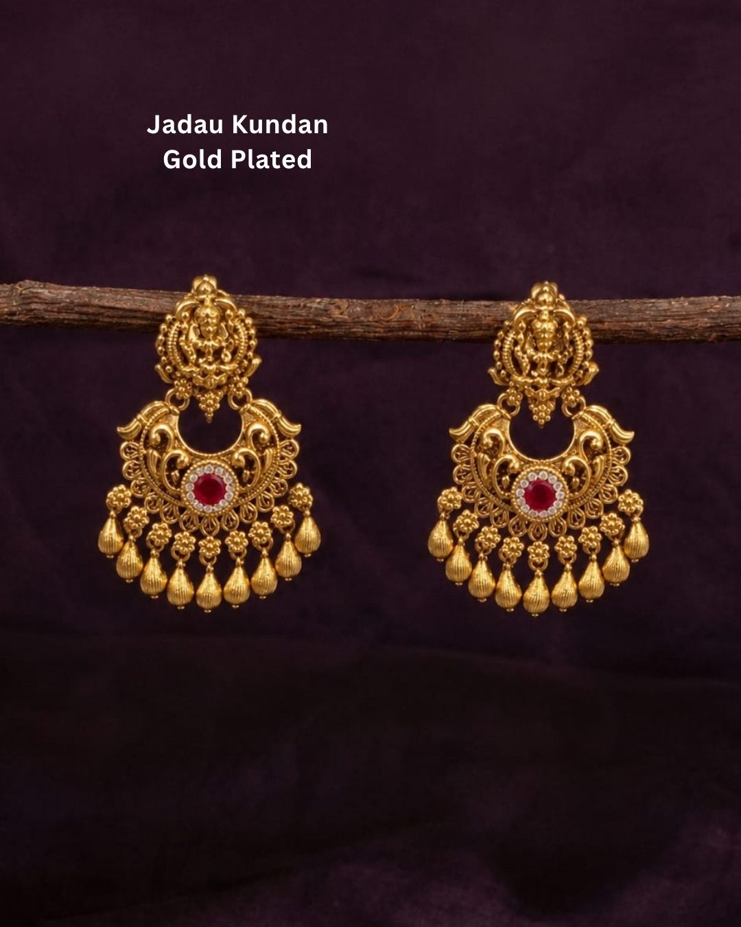 Gold-plated Laxmi Set jewelry necklace and matching earrings displayed on a dark red velvet bust. The necklace features intricate gold filigree, red and green stone accents, and rows of white faux pearls.