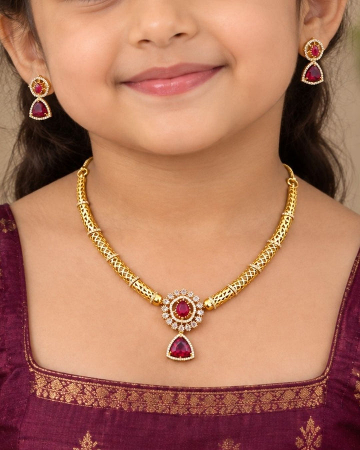 Gold-plated necklace and matching earrings set displayed on a black jewelry bust. The necklace features a textured gold chain with a central teardrop pendant and matching drop earrings, embellished with green stones and small clear stones.