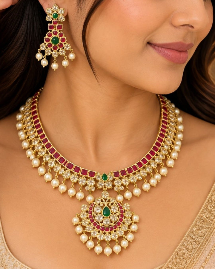 Traditional style 18K gold plated choker necklace set designed with a red stone border band, white crystal outlines, a central crescent pendant, and clean rows of hanging white pearl drops that give a neat traditional look for festive celebrations, poojas, and weddings.
