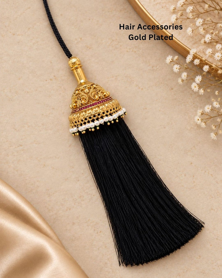 Elegant gold plated Jada Gantalu with intricate temple-inspired craftsmanship, ruby stone accents, pearl detailing, and long black tassels, perfect for bridal and festive hairstyles.