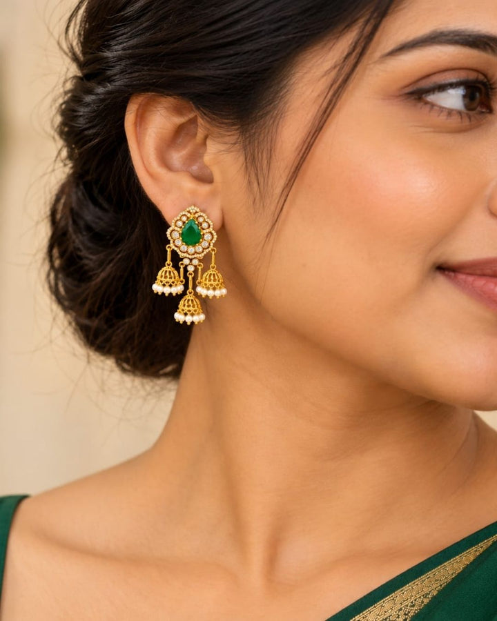 Gold plated zircon diamond jhumka earrings featuring ruby red teardrop stones, clear sparkling stones, and multiple pearl-decorated gold jhumka hangings.