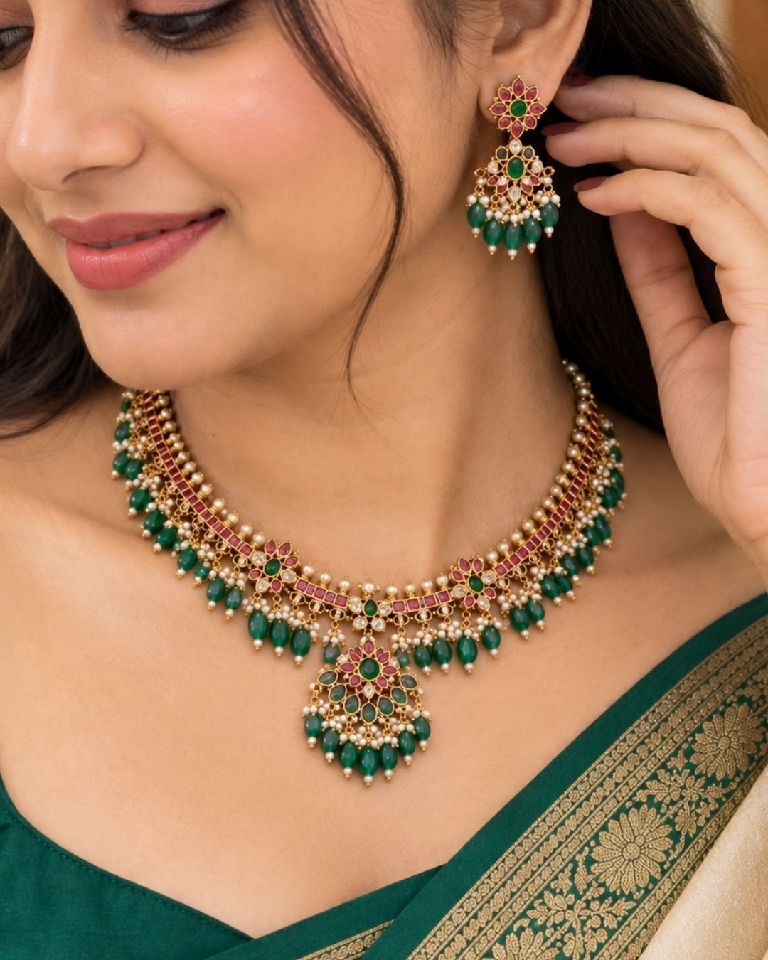 Traditional gold plated designer necklace and earrings set featuring intricate floral motifs with green and ruby-colored stones, sparkling white stones, pearl embellishments, and multiple green bead drops, perfect for festive, wedding, and traditional occasions.