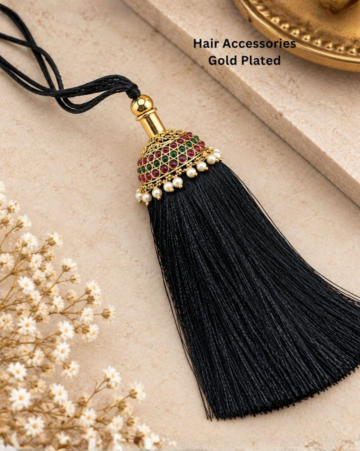 Elegant gold plated Jada Gantalu featuring a dome-shaped design with ruby and green stones, delicate pearl drops, and a long black thread tassel, perfect for bridal and festive hairstyles.