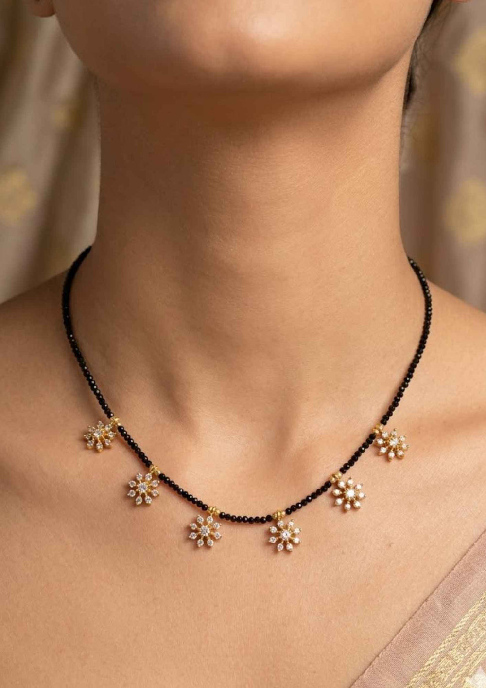 South Indian woman wearing Gold Plated Sankranti Mangalsutra with neatly arranged black beads chain and simple traditional floral pendant that gives a neat and graceful jewelry look. The mangalsutra shows lightweight comfort, smooth finishing, sweat proof quality, anti-fade colour, skin-friendly finish, and is suitable for daily use, office wear, family functions, and festivals.