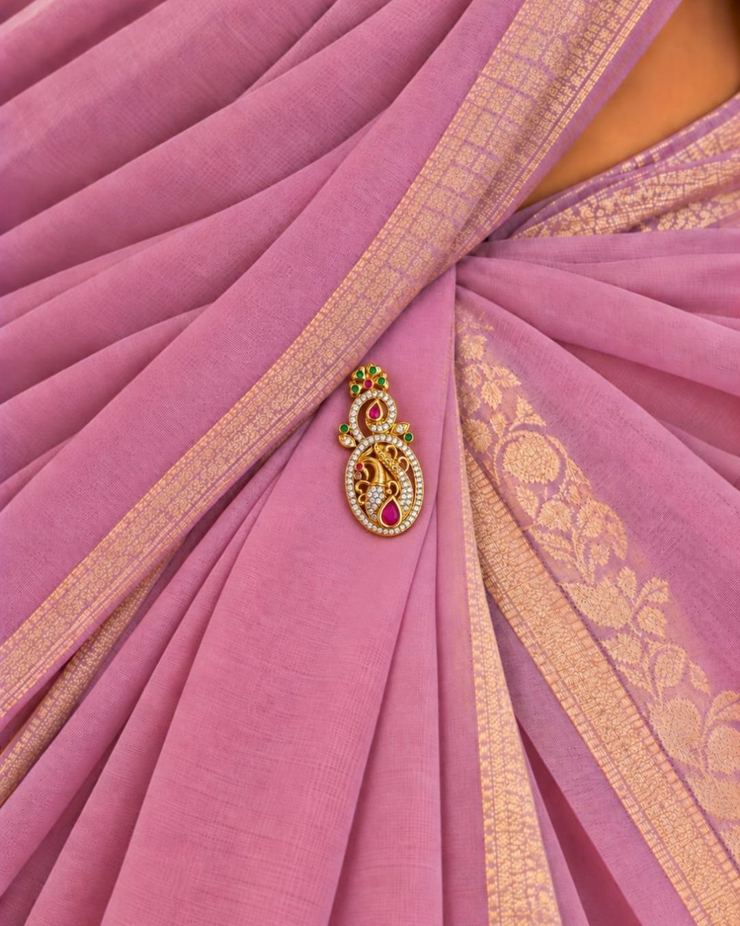 Pair of gold plated peacock design saree pins displayed on a light wooden surface, showing decorative front designs and secure pin-back fastenings.